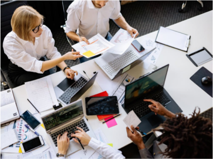 image from aerial view of group of adult professionals working on project with laptops and paper documents